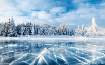 Blue ice and cracks on the surface of the ice. Frozen lake under a blue sky in the winter. The hills of pines. Winter. Carpathian, Ukraine, Europe. Naklejkomania - zdjecie 1 - miniatura