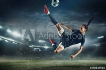 Young female soccer or football player with long hair in sportwear and boots kicking ball for the goal in jump at the stadium. Concept of healthy lifestyle, professional sport, hobby, motion, movement Naklejkomania - zdjecie 1 - miniatura