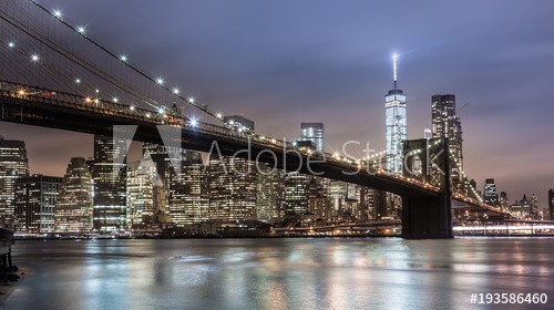 Brooklyn bridge and New York City Manhattan downtown skyline at dusk with skyscrapers illuminated over East River panorama.