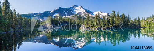 Volcanic mountain in morning light reflected in calm waters of lake.