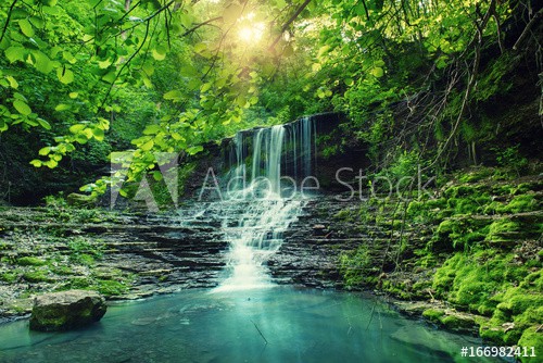 Beautiful mountain rainforest waterfall with fast flowing water and rocks, long exposure. Natural seasonal travel outdoor background with sun shihing - zdjęcie 1