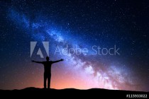 Night landscape with Milky Way. Silhouette of a standing young man with raised up arms on the mountain. Beautiful Universe. Travel background with blue night starry sky Naklejkomania - zdjecie 1 - miniatura